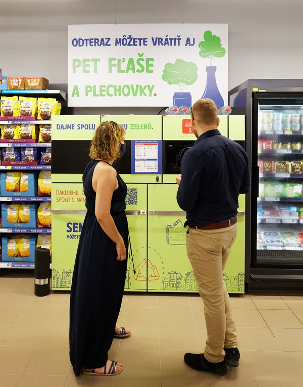 a man and a woman standing in front of a reverse vending machine